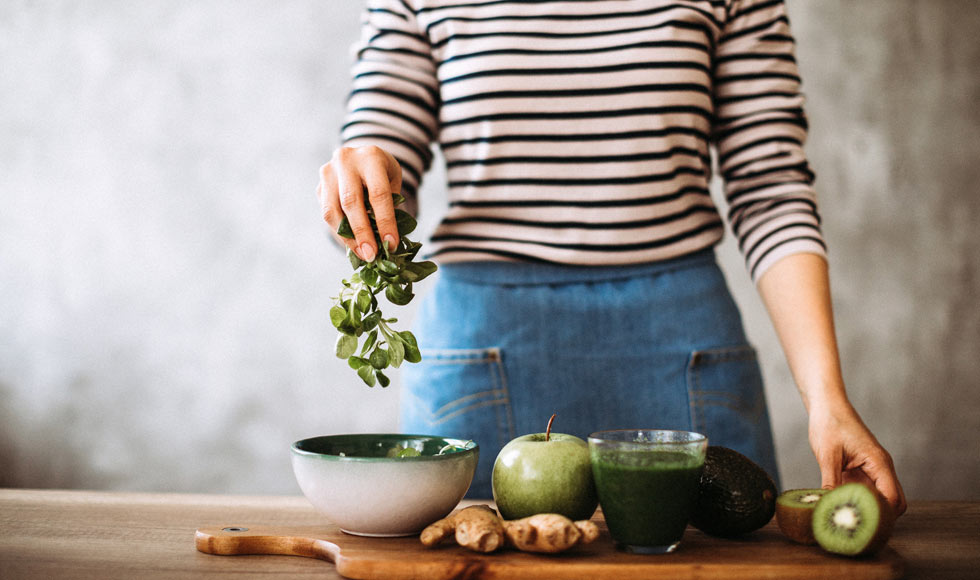 Woman preparing green smoothie at home on cutting board
