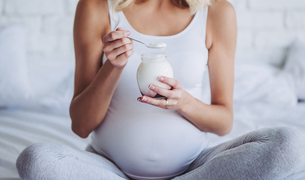 Pregnant woman sitting on the bed eating yoghurt