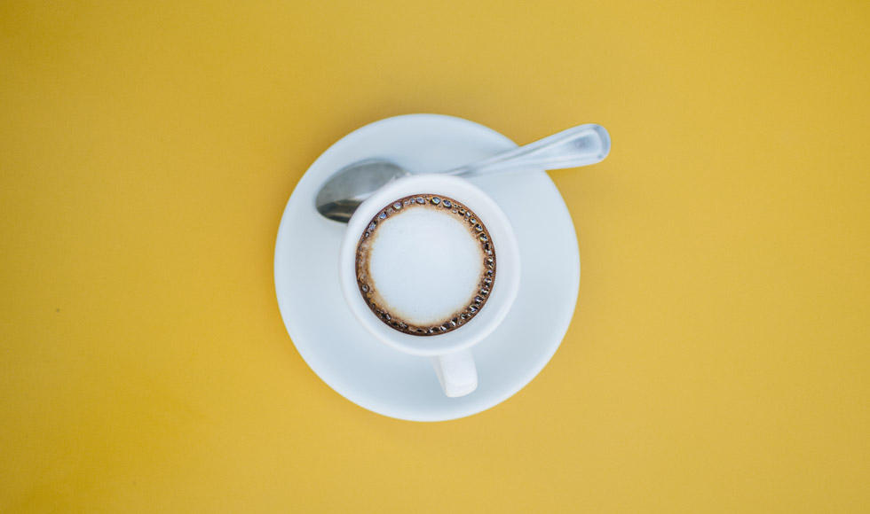 Flat lay of a cup of coffee on a yellow background