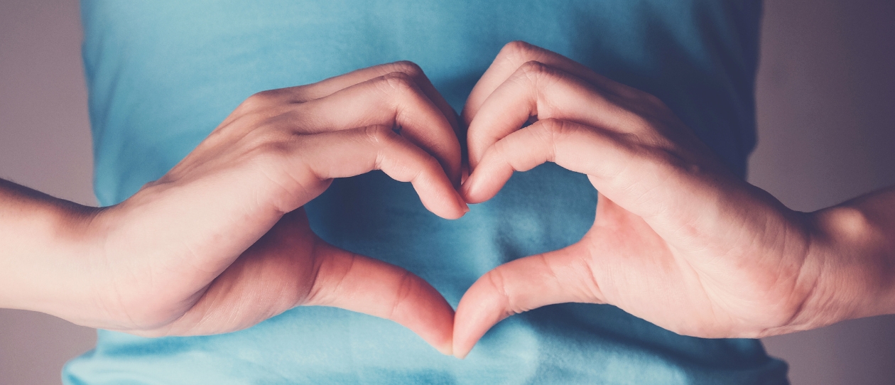 Two hands forming a heart across the abdomen