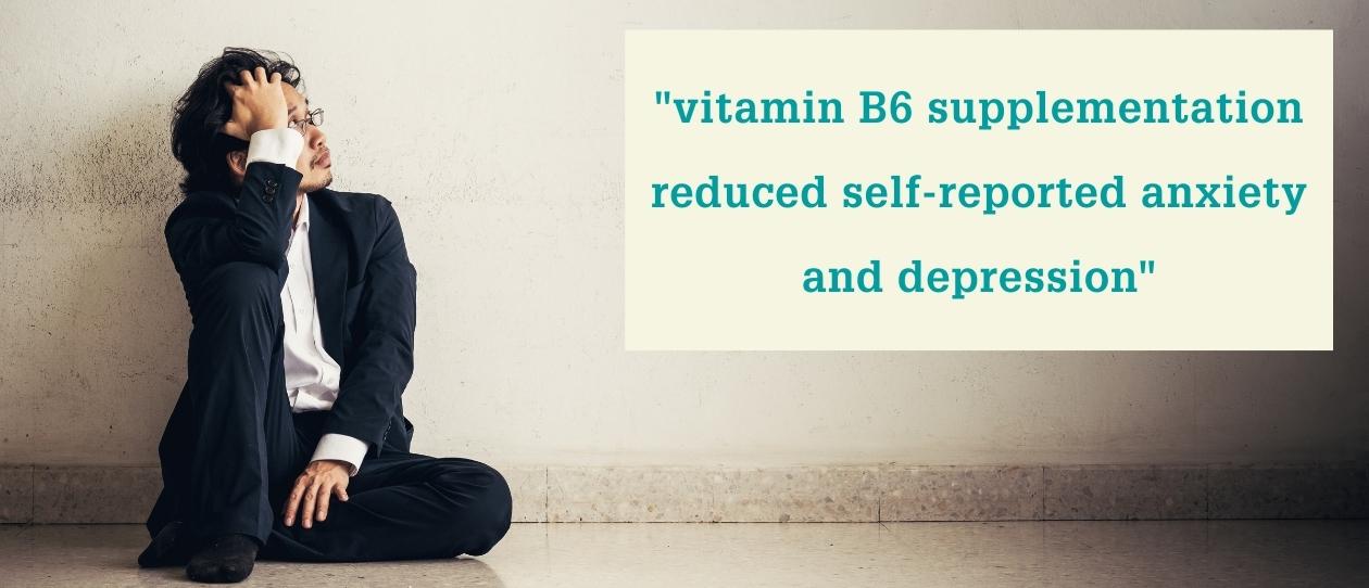 Man in suit sitting against wall with hand on head looking at text referring to vitamin B6 supplementation for anxiety and depression