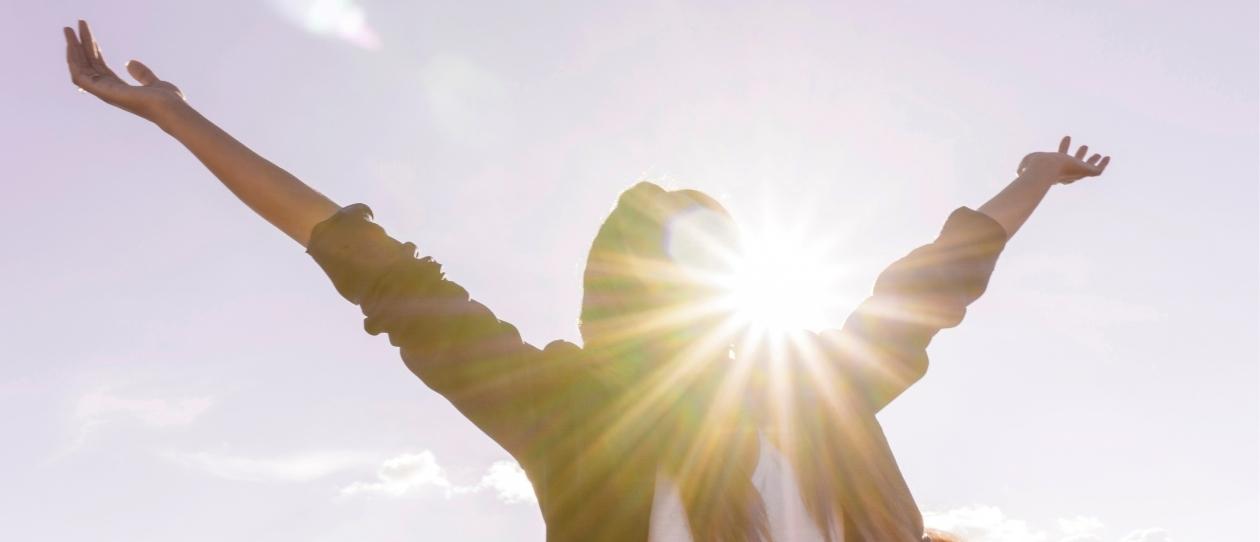 Person raising arms to sky in the sunshine for vitamin D